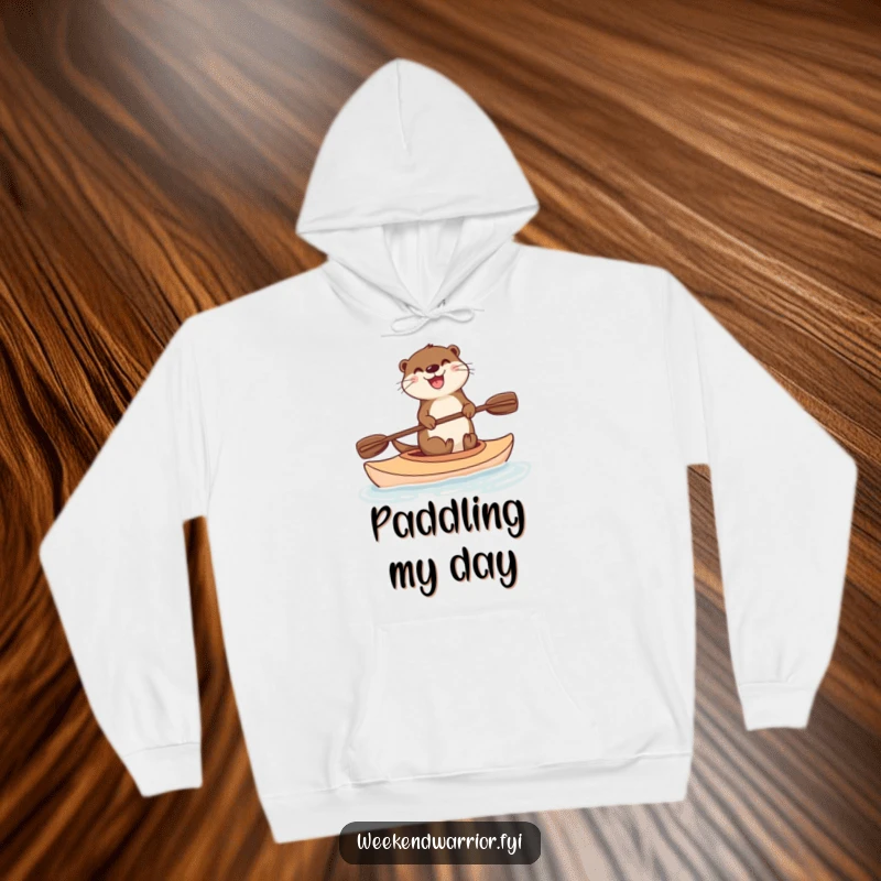 Funny hoodie featuring a happy otter enjoying a kayak ride, paddle ready, radiating warmth and amusement on a cool day.